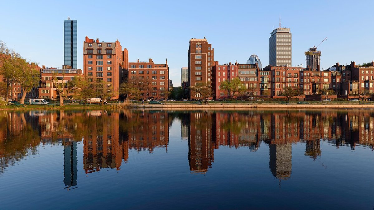 Joggers and cyclists on the Charles River Esplanade with sailboats on the river and the Boston skyline in the background