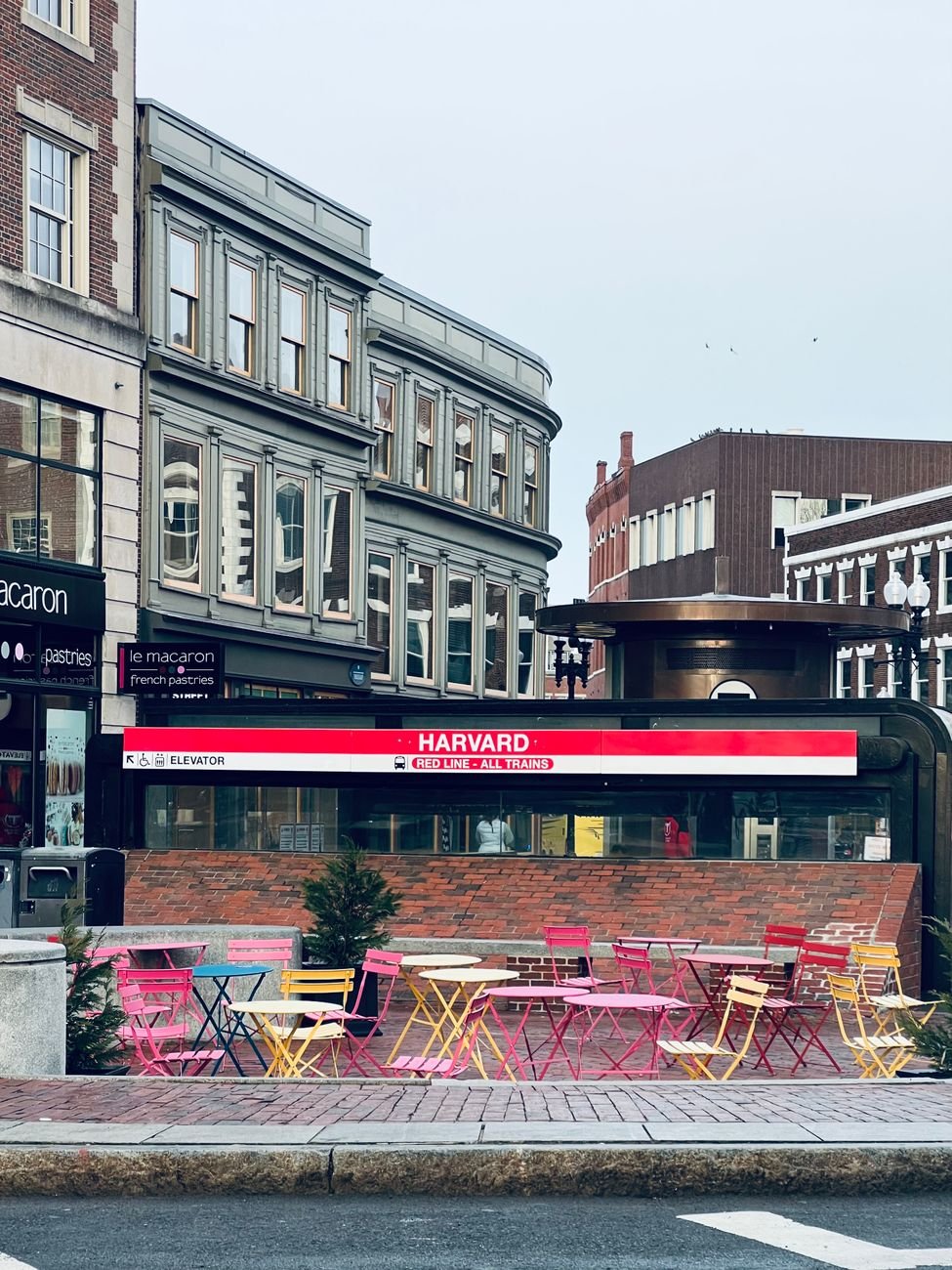 Harvard Square with the MBTA station headhouse, cafe tables, and brick storefronts